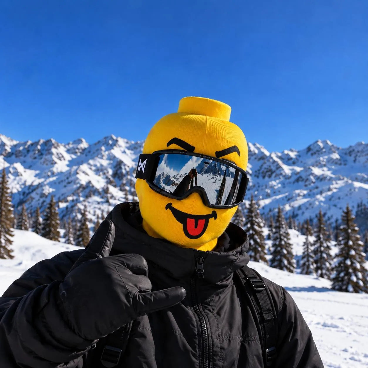 Yellow knit ski mask with a tongue-out face, worn with ski goggles in the mountains